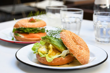 Avocado egg bagel on white plate on a table in a cafe. top view