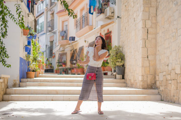 Fototapeta na wymiar Asian girl taking self portrait on the street - young happy and attractive Asian Chinese woman visiting Seville in Spain taking selfie enjoying beautiful old city tour cheerful