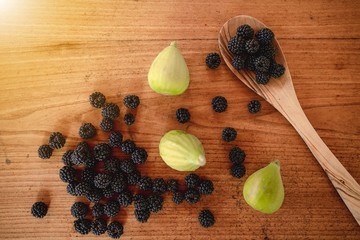 Top view three ripe figs, many blackberries and a wooden spoon on a wooden table. Seasonal summer fruits, organic and healthy food.