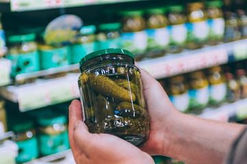 The guy in the supermarket holds a glass jar of cucumbers.