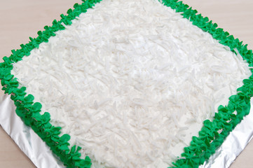 Birthday cake decorated with green icing and grated coconut. Isolated on wooden table background....