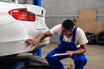 A mechanic in overalls inspects a car for damage
