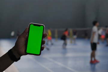 close up hand showing green screen smart phone in indoor stadium.Defocused people playing badminton