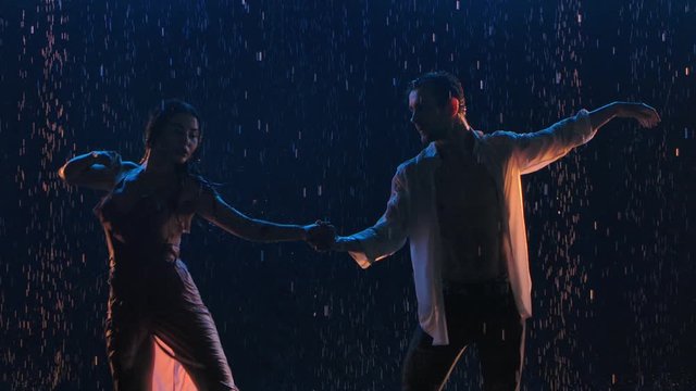 Sensual passionate dance of a couple in love at night in the rain. Contact of wet hot bodies. Silhouettes of two lovers. A love story expressed in dance. Close up. Slow motion.