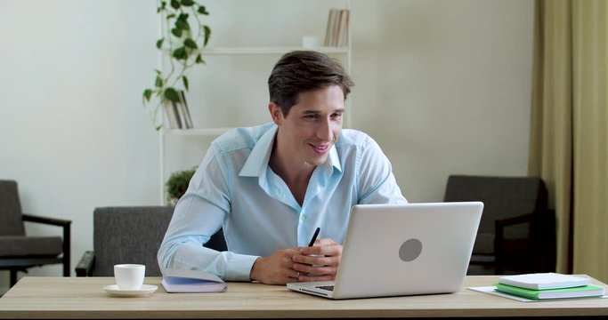 Smiling classic man sits at table at home in office, uses laptop web camera to communicate with family friends, actively speaks on video conference network gestures with hands, answers Internet call