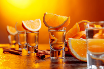 Glasses of gold tequila with orange slices and cinnamon sticks on a table in bar.