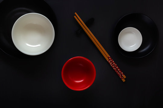 White, black and red empty plates with chopsticks in an oriental style lie on a dark table in a minimalist composition. Top view