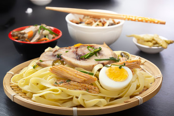 Noodles with pieces of meat and an egg in a bamboo plate on a dark table. Asian food concept.