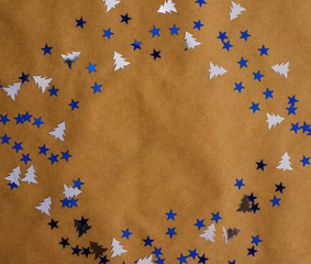 Festive sequins are scattered on the Kraft paper in the shape of a circle. New year holiday background.