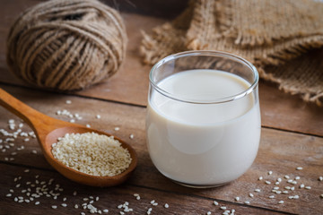 Sesame milk in glass and white sesame seeds on wooden spoon.