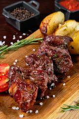 Beef shashlik garnished with vegetables and baked potatoes. In the background are sauces for meat.
