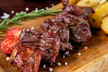 Beef shashlik garnished with vegetables and baked potatoes. In the background are sauces for meat.