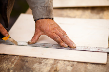 Senior elderly carpenter using a straightedge to draw a line on a board.