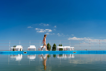 teenage girl in swimsuit goes along pool background sky