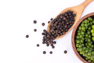 Closeup fresh green pepper in wooden bowl and black peppercorn seeds ( piper nigrum) in spoon isolated on white background. Top view. Flat lay.