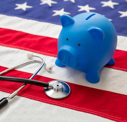 US of America health budget. Medical stethoscope and piggy bank on a USA flag, closeup view.