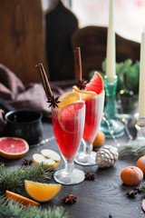 Christmas lemonade on a table with different New Year decorations. Red drink on the festive table. Glass toys, garland and candles. Live spruce branches.