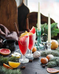 Christmas lemonade on a table with different New Year decorations. Red drink on the festive table. Glass toys, garland and candles. Live spruce branches.