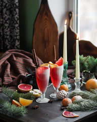 Christmas lemonade on a table with different New Year decorations. Red drink on the festive table. Glass toys, garland and candles. Live spruce branches.