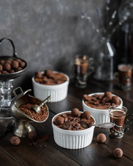 Chocolate mousse in a white ceramic bowl, decorated with truffles, sesame seeds and sweets on a wooden table.