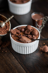 Chocolate mousse in a white ceramic bowl, decorated with truffles, sesame seeds and sweets on a wooden table.