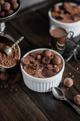 Chocolate mousse in a white ceramic bowl, decorated with truffles, sesame seeds and sweets on a wooden table.
