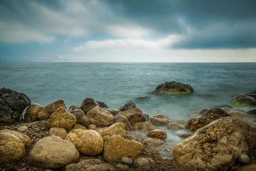 Sea beach and coastal stones in the water in the evening. Long exposure landscape.