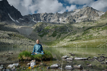 Fototapeta na wymiar Young woman sits in yoga lotus position against the turquoise lake in the mountains. Extreme hiker girl rest in the wild nature. Trekking lifestyle. Domestic local hike, tourism, travel