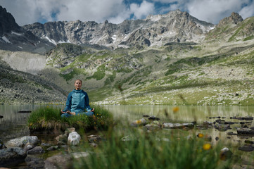 Young woman sits in yoga lotus position against the turquoise lake in the mountains. Extreme hiker girl rest in the wild nature. Trekking lifestyle. Domestic local hike, tourism, travel
