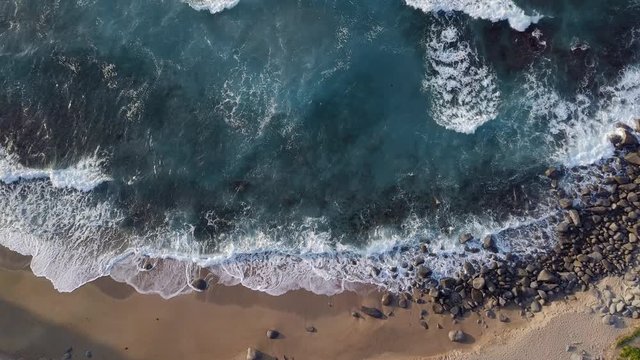 Waves consecutively lapping onto the shore and white bubbles remaining on the surface of beautiful blue ocean.