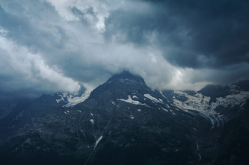 Gloomy mountain top landscape with thunder cloudy sky, rocky ranges and peaks with glaciers and snow fields. Rainy day in wild nature. Belalakaya, Dombay, Caucasus
