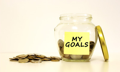 Glass jar with coins for savings. The inscription on the note paper MY GOALS. Financial concept.