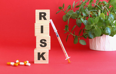 The words RISK is made of wooden cubes on a red background with medical drugs. Medical concept.