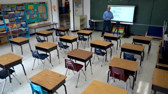 Teacher teaching to a phone video camera using an interactive whiteboard in an empty classroom.