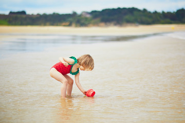 Fototapeta premium Adorable toddler girl on the sand beach at Atlantic coast of Brittany, France