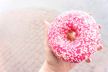 Pink doughnut in woman's hand with copy space. Dessert festive. donut with a pink chocolate frosting. Breakfast and hen-party concept. 