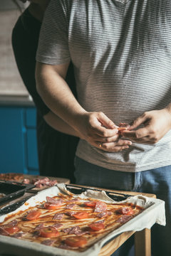 Male and female hugs in the home kitchen while cooking. Romantic kitchen in a city apartment. The lifestyle of modern youth. Young couple hugs and prepares pizza. Image with selective focus. 