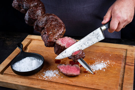 Traditional barbecue dry aged wagyu Brazilian picanha from the sirloin cap of rump beef sliced by a chef directly from the skewer as close-up on a wooden cutting board