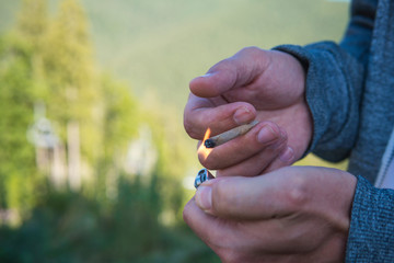 Close-up of young man smoking marijuana joint outdoors. Hemp blunt in the male hand. Cannabis is a...