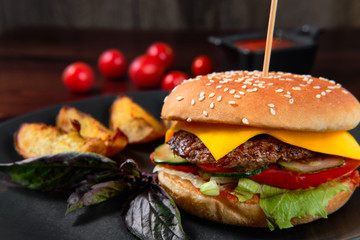 A classic burger with fresh herbs and a juicy cutlet. Close up view of fresh tasty beef burger and french fries with seasoning on rustic table.