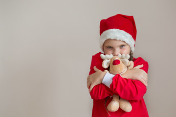 Happy girl in santa costume with deer toy on light gray background 