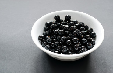 Fresh black currant on a snow-white plate, which stands on a black background. Side view