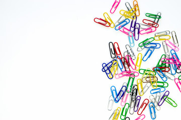 Multicolored metal and plastic paper clips on a white background, collected in a pile on the right