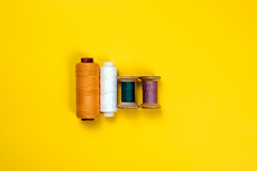 Four spools of colored thread lie in a row against a bright yellow background. View from above