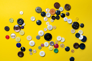 Multi-colored plastic buttons lie chaotically on a bright yellow background