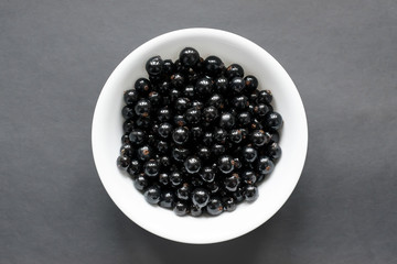 Fresh black currant on a snow-white plate, which stands on a black background. View from above