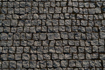 Close-up View of Surface of Small Grey Granite Setts, many irregular rough square stone paving blocks with brown sand jointing
