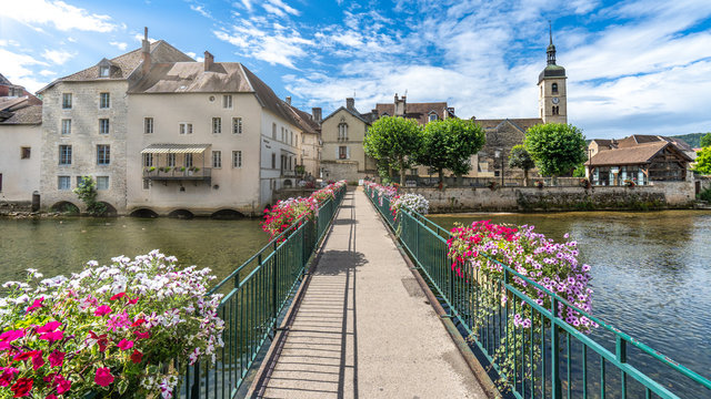 Blumen geschm&uuml;ckte Fussg&auml;ngerbr&uuml;cke mit Blick auf eine Kirche, Ornans, Bourgogne-Franche-Comt&eacute;, Frankreich