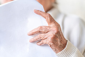 Fototapeta premium Nahaufnahme Hand, alte Frau mit faltigen Händen liest einen weißen Brief