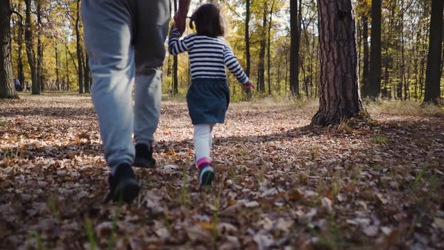 Father with his little daughter running in the autumn park slow motion